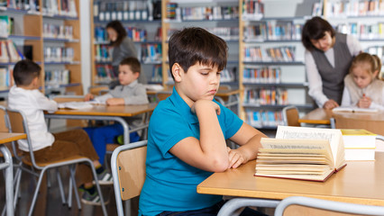 Fototapeta na wymiar Tween boy reading textbooks in school library