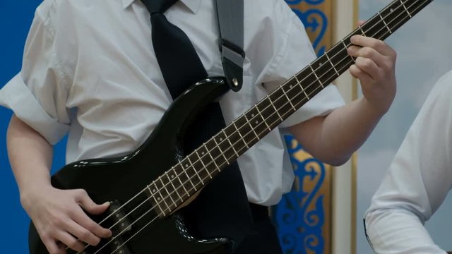 The fingers of the right hand are pulling the strings. Concept musical theme of youth. A teenager in a white shirt with rolled up sleeves plays an electric bass guitar.Close-up.