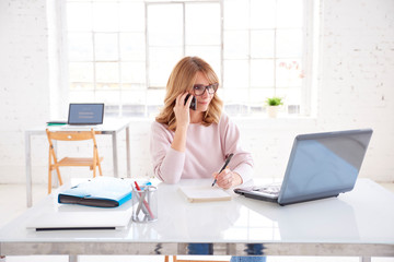 Businesswoman talking with somebody and working on laptop in the office