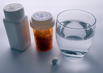 Several bottles with diverse medication next to a glass of water, conceptual image