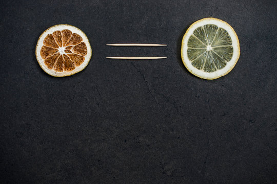 Dried slice of lemon and fresh one that have equal sign between them on a black background.