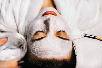 Close up portrait of a lovely woman doing a rejuvenation white mask with hyaluronic acid in a spa salon.