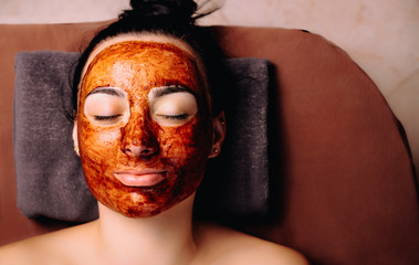 Close up of a beautiful female resting with close eyes with a chocolate mask on her face. Spa procedures with chocolate .