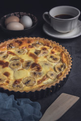 Banana custard tart with cup of coffee, spatula and ingredients. Vertical