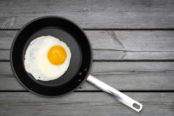 Top view of a sunny side up fried egg in a black pan on wooden rustic table with copy space.
