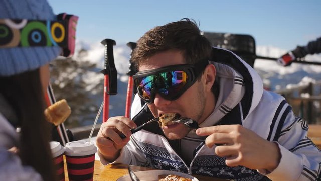 Lunch break at a ski resort. Young couple having lunch in restaurant outdoors in the mountains and communicate with each other.