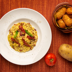 risotto with dried tomatoes, asparagus and bacon with side dish of potato croquettes from top