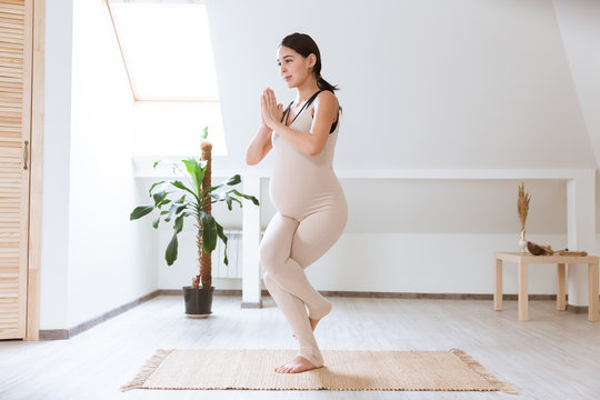 Young pregnant yoga woman working out at home doing prenatal Tree posture, Vrksasana yoga pose. Healthy Pregnancy concept. Pregnant Namaste gesture