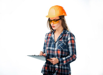 Attractive woman builder in orange helmet and protective glasses with folder in hand writing on white background. Pretty engineer in shirt writing with ballpoint pen on black folder
