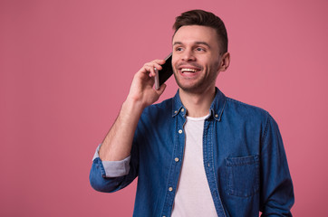 Handsome modern casual man is talking on smart phone isolated on pink background