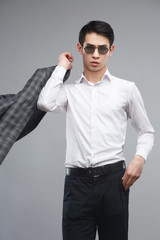 Young asian man in sunglasses holding a jacket in his hands isolated on gray background.