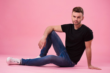 Beautiful stylish confident and serious man in black t-shirt is posing on pink background