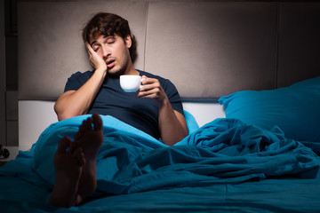 Young handsome man suffering from insomnia in bed