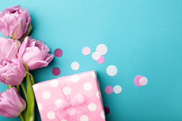 Gift box wrapped in polka dot paper and pink tulip flowers on blue background decorated with...