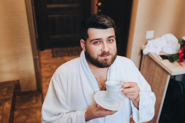 Portrait of a stylish bearded groom. A young man in a white coat with a large beard is drinking...