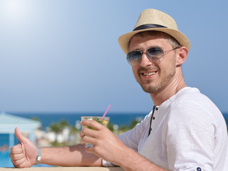 European Man in sunhat and sunglasses with glass of long drink cocktail. He is standing on the...