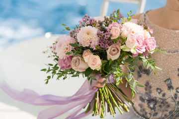 the bride holds a pink and lilac wedding bouquet in her arms against the background of the sea