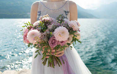 the bride holds a pink and lilac wedding bouquet in her arms against the background of the sea