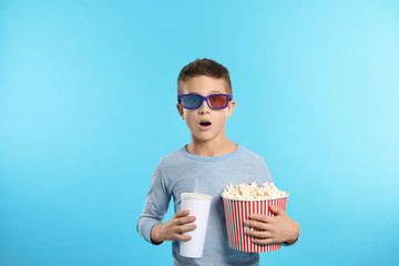 Fototapeta premium Emotional boy with 3D glasses, popcorn and beverage during cinema show on color background