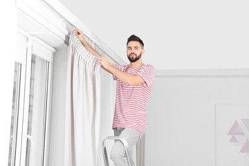 Fototapeta na wymiar Young handsome man hanging window curtain in room
