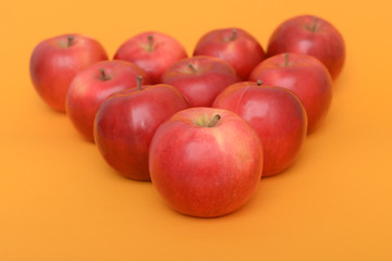 Big piramid of red apples on the orange background