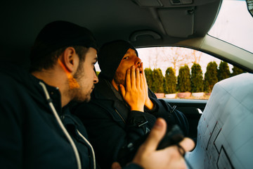 Two armed bandits sitting in a car planning their next robbery, while counting on a stopwatch the...