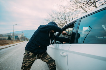 Carjacker aggressively attacking a car owner with a gun, trying to extort money.