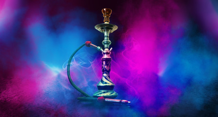 Smoking hookah on the background of an empty room. Multicolored neon light. Searchlight, laser blue...