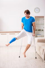 Leg injured young man with crutches at home 