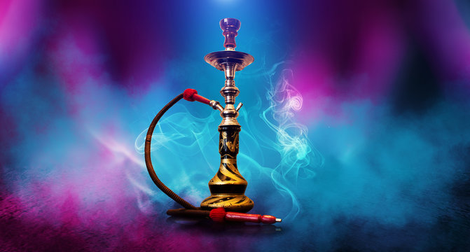 Smoking hookah on the background of an empty room. Multicolored neon light. Searchlight, laser blue and pink rays, smoke.