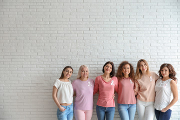 Group of women with silk ribbons near brick wall, space for text. Breast cancer awareness concept