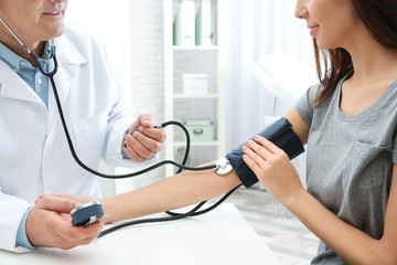 Young woman visiting doctor in hospital, closeup. Measuring blood pressure and checking pulse