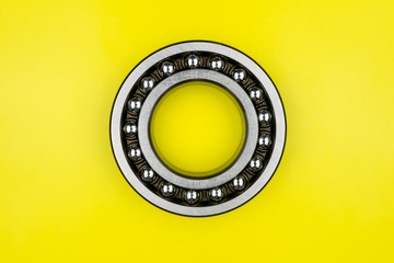 Ball bearing lying on a yellow background with copy space on the sides. Flat view from above.