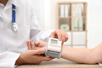 Doctor checking mature woman's pulse with medical device in hospital, closeup