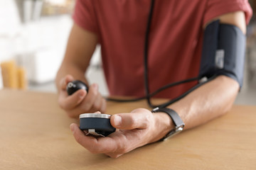 Man checking blood pressure with sphygmomanometer at table indoors, closeup. Cardiology concept
