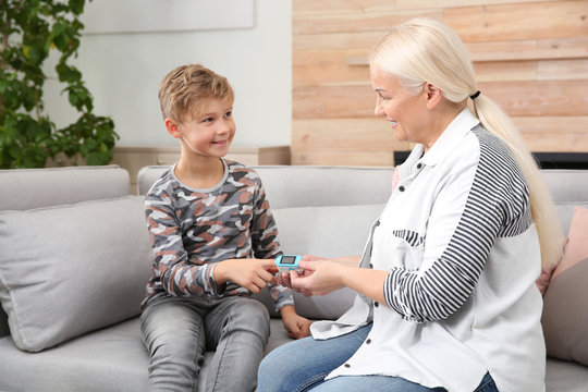 Mature woman checking little boy's pulse with medical device at home