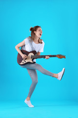 Young woman playing electric guitar on color background