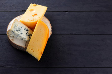 Hard cheese and blue cheese on wooden stand. Different types of cheese on black boards. Swiss cheese and dorblu on dark background