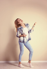 Young woman playing air guitar near grey wall