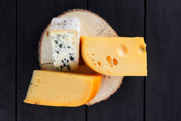 Hard cheese and blue cheese on wooden stand. Different types of cheese on black boards. Swiss cheese and dorblu on dark background