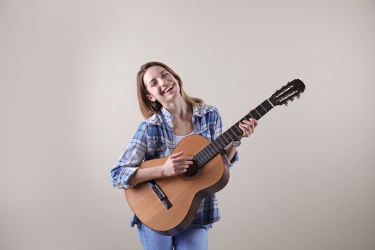 Young woman playing acoustic guitar on grey background