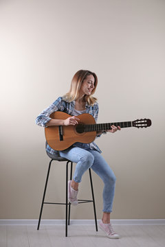 Young woman playing acoustic guitar near grey wall