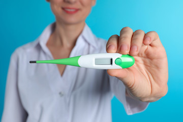 Female doctor holding digital thermometer on color background, closeup. Medical object