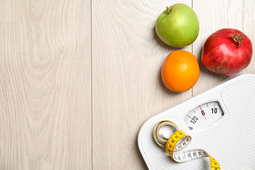 Flat lay composition with scales, measuring tape, fruits and space for text on wooden background. Weight loss