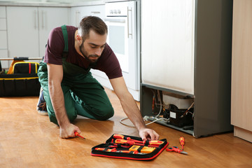 Male technician in uniform repairing refrigerator indoors