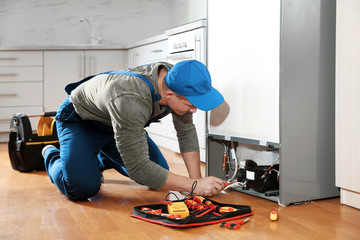Male technician in uniform repairing refrigerator indoors