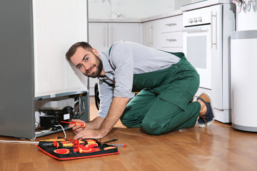 Male technician in uniform repairing refrigerator indoors