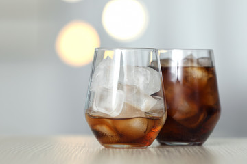 Glasses of cola with ice on table against blurred background