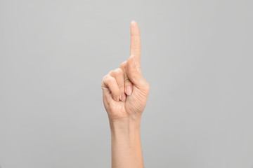 Woman showing number one on grey background, closeup. Sign language