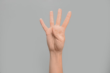 Woman showing number four on grey background, closeup. Sign language
